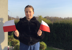 Uczennica trzyma w dłoniach dwie małe flagi Polski.
